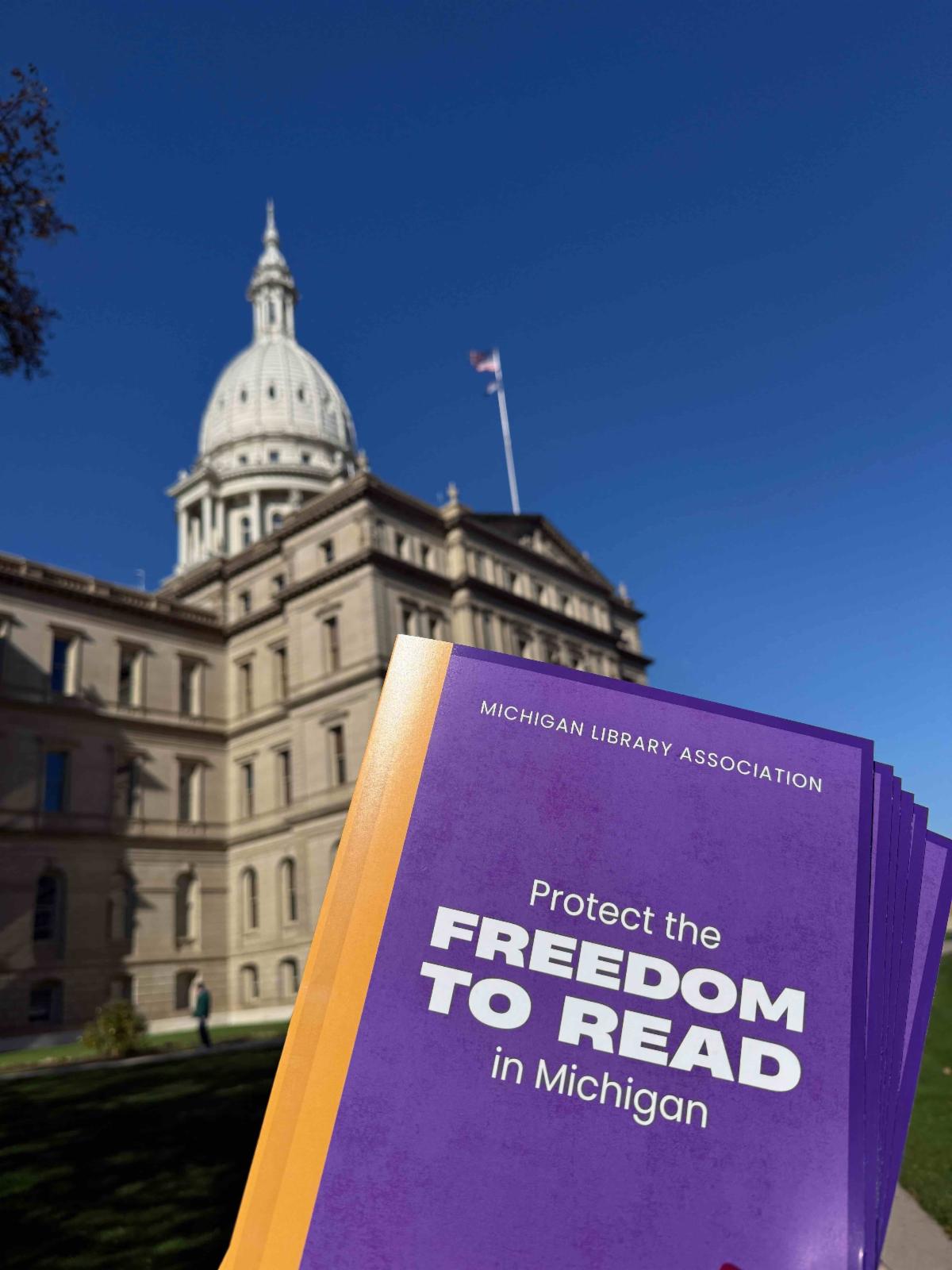 Copies of the petition, delivered in purple folders with "Protect the Freedom to Read in Michigan" on the cover, being held up in front of the Michigan Capitol Building