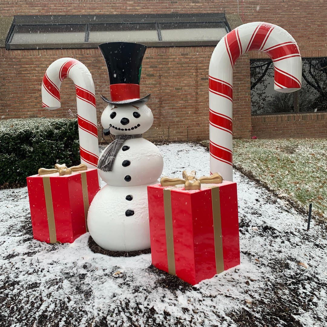 snowman and candy cane decoration on the lawn in front of a brick building